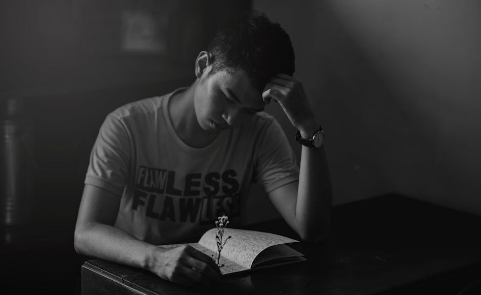 Contemplative young man reading a notebook in a dimly lit room.