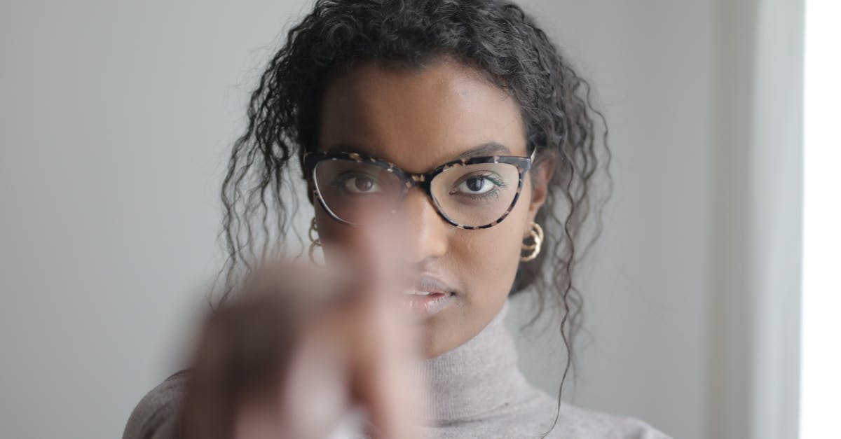 Young woman pointing at camera with focus on her face wearing glasses and a casual outfit.