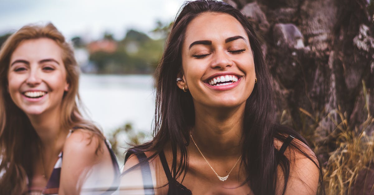 Two women happily laughing together outdoors by a serene lakeside.